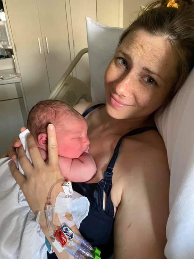 Smiling new parent in hospital bed holding newborn