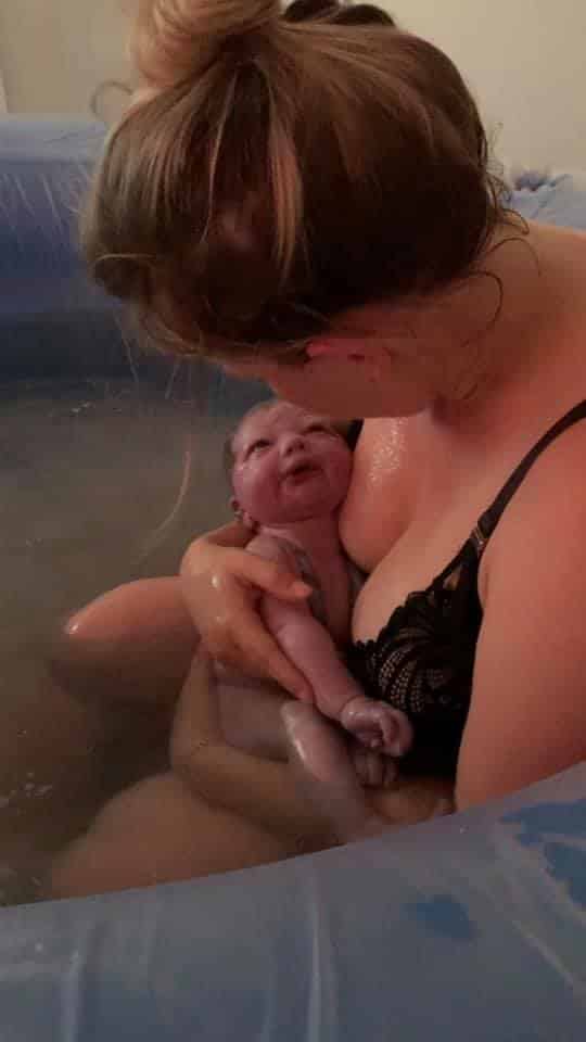 Sarah in her birthing tub just after giving birth holding and looking at her baby.