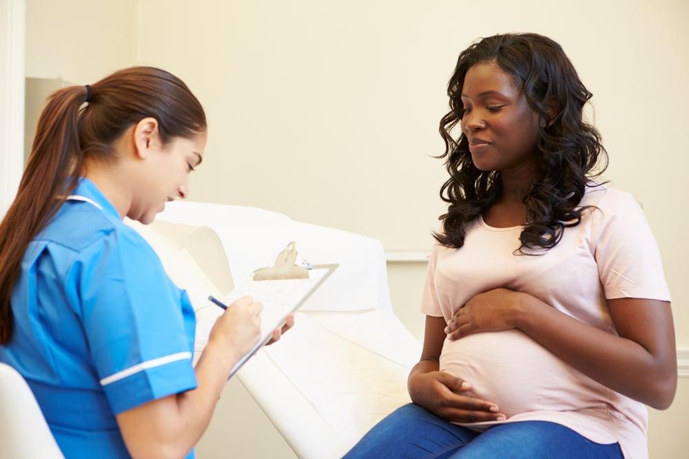 Nurse in a hospital taking notes talking to pregnant person